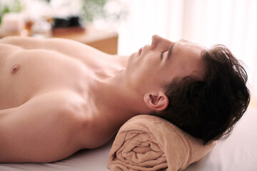 Fototapeta na wymiar Young man relaxing in beauty salon after getting rejuvenating face and neck massage