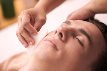 Obraz na płótnie Canvas Cosmetologist using gua sha when massaging face of man