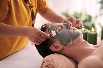 Obraz na płótnie Canvas Cosmetologist giving rejuvenating face massage to man after applying face mask