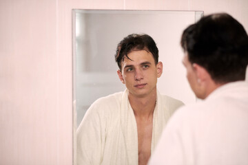 Portrait of young man wet after morning shower looking at bathroom mirror