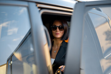 Portrait of an elegant business lady in black in luxury car, view through the door. Concept of...