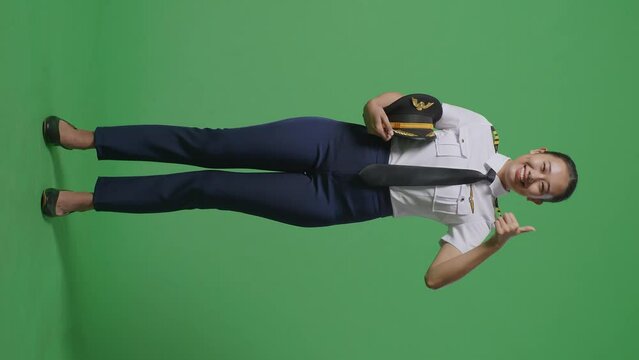Full Body Of Asian Woman Pilot Smiling And Showing Thumbs Up Gesture To Camera While Standing In The Green Screen Background Studio
