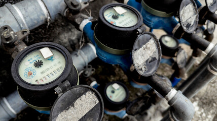 Several analog water meters installed outside an apartment building or other commercial property. Water bill and usage separated per tenant.