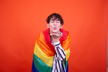 Funny curly guy posing in the studio on an orange background with a gay flag.