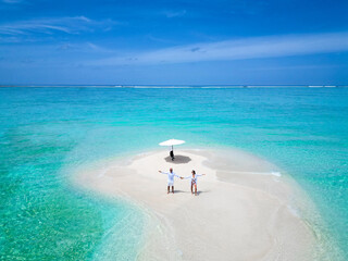 Top aerial drone view of beautiful couple in white shirts, stands on the island's shore, holding...