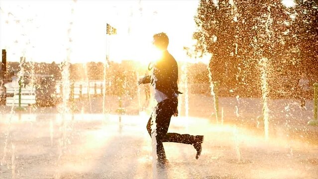 Young Happy Businessman Dancing Cheerful in Water Fountain at Sunset