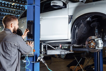 Tire change, car service and vehicle repair. Mechanic elevators car on hoist in service station.