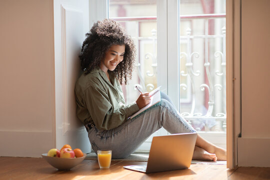 Black Woman Using Laptop Taking Notes In Notebook At Home