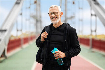 Positive retired sportsman standing on walking bridge, going home