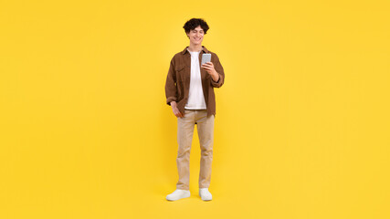 Fototapeta na wymiar Young Man Using Mobile Phone Browsing Internet Over Yellow Background
