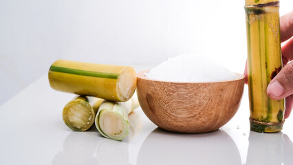 White granulated sugar and sugar cane stalks isolated on a white background.
