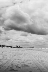 Coastline with a set of tire tracks leading your eye through the photo against a dramatic cloudy sky done in black and white.