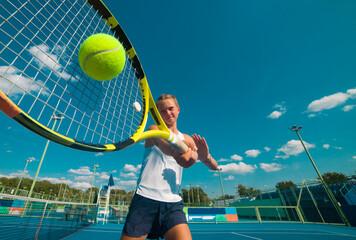 A girl plays tennis on a court with a hard blue surface on a summer sunny day. focus on tennis ball 