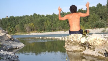 Man 40 years old does yoga meditation on a rock in the river - lifestyle in nature - relaxing during the summer holidays 