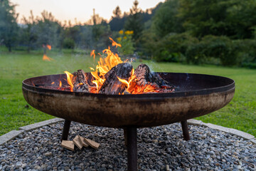 A portable fireplace with bright burning firewood making sparks and smoke at the backyard or garden...