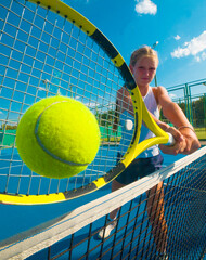 girl tennis player stands leaning on the tennis net on the court on a bright sunny day