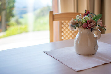 Home furnishings with dining table and flower pot. Window with outdoor light illuminating the living room.