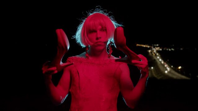 Drag queen holding her high-heeled shoes in red lighting