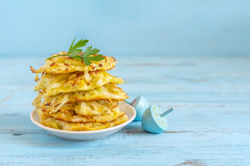 Cabbage fritters or latkes for Jewish holiday Hanukkah on blue wooden background with copy space. - obrazy, fototapety, plakaty