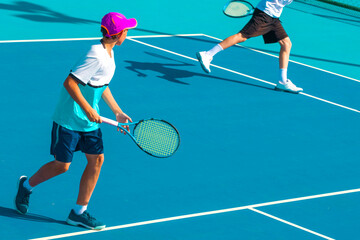 A tennis player plays tennis on a court with a hard blue surface on a summer sunny day