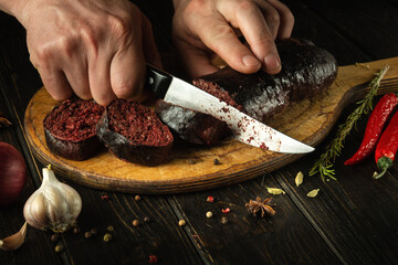 Slicing blood sausage by the hands of a chef on a cutting board. Cooking national dish on the...