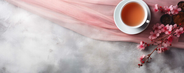 Obraz na płótnie Canvas Delicious hot spring drink in a white cup on a pink fabric with a branch of cherry blossoms, promo banner for advertising. Minimalistic grey textural background. Сopyspace