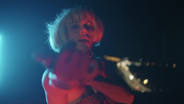 Drag Queen in a blonde wig flirts with the viewer in red lighting
