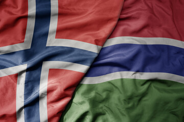 big waving national colorful flag of norway and national flag of gambia .