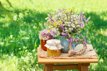 Jars with honey and bouquet of wild flowers in the garden.
