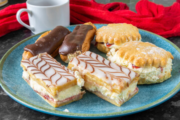 Selection of cakes including chocolate eclairs, cream pastry slices and scones with cream and jam...