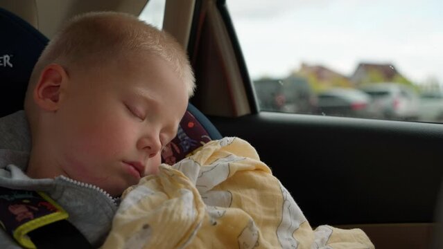 Portrait of a cute sleeping baby in a child safety seat in a car. A boy rests in a child seat during a road trip in a car with his parents. Ensuring child safety while driving.