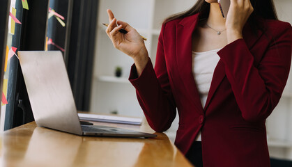 Asian Businesswoman Using laptop computer and working at office with calculator document on desk, doing planning analyzing the financial report, business plan investment, finance analysis concept.