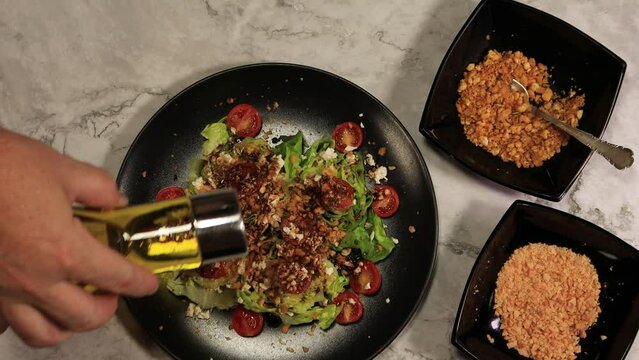 4K salad with cherry tomatoes, cheese and nuts on a black plate with vinegar and two black bowls on a gray marble table, silver spoon and olive oil, zenithal picture