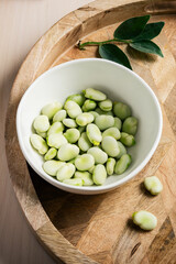 Bowl of green fava beans on a wooden tray.
