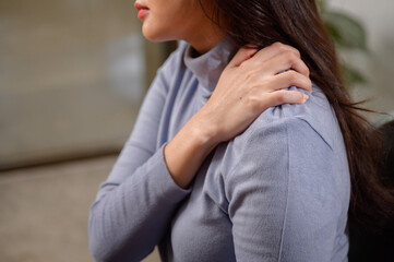 Close-up of young Asian woman having pain in shoulder and neck while using laptop computer at home...