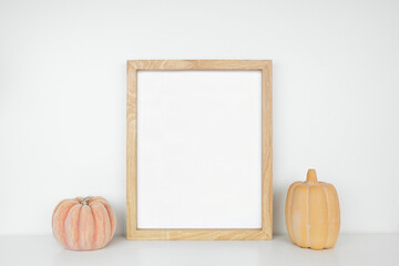 Mock up portrait wooden frame with autumn pumpkin decor on a white shelf against a white wall. Copy...