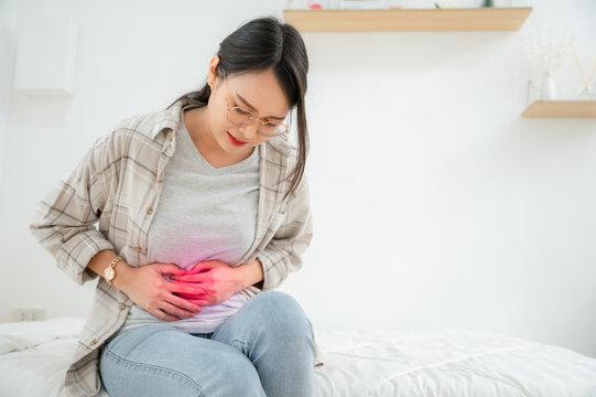 Asian woman with abdominal pain sitting in bed at home She was suffering from severe abdominal pain. Stomach discomfort and food poisoning diarrhea