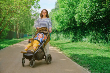 The child and mother are taking a leisurely stroll through the park with their carriage. Kid aged about two years (one year eleven months)