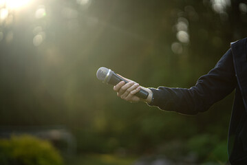 The hand extends the microphone. Performing a song in the fresh air. Karaoke party on the street.