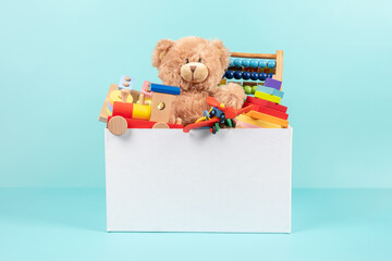 Toy box full of baby kid toys. Container with teddy bear, fluffy and educational wooden toys on light blue background. Cute toys collection for small children. Front view