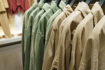 Green and brown long sleeve shirts hang on hangers in a clothing store.