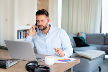 Mid aged man sitting at home and using laptop and smartphone for work