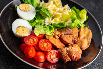 Fototapeta na wymiar salad chicken liver, pasta salad , tomato, green leaf lettuce, boiled egg, farfalle snack meal food on the table copy space food background rustic top view