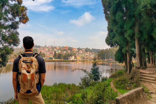 Male tourist backpacker enjoys view of the scenic Mirik lake with cityscape at Darjeeling, India.