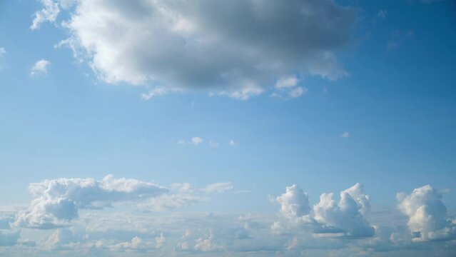 Fluffy white clouds gracefully drift across the daytime blue sky, creating a mesmerizing timelapse.