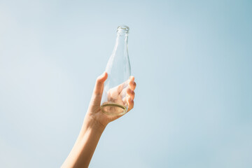 Recyclable glass bottle held in hand up on sky background. Hand holding plastic waste for recycle...