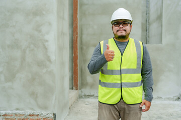 Asian architect, construction supervisor. wearing a white safety helmet Stand and show your thumb towards the camera. Show confidence At the house construction site. man wearing reflective vest