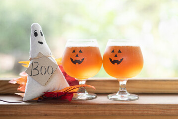 Pumpkin beer in jack-o-lantern glasses sitting alone side a ghost with a tag, 