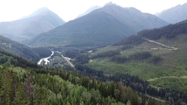 Aerial Valley Landscape View - Pan Right - British Columbia Rocky Mountains. Valley scenery: Mountains, Lake, Clouds, Sky, Trees, Forest. Beautiful British Columbia.