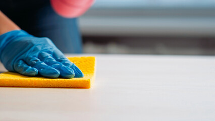 Cleaning company. Janitor services. Housekeeper hand in protective gloves washing light table furniture with surface wiping sponge carefully.